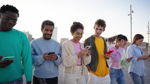 A group of multiracial young people walking using mobile cell of the city street while looking and using their smart phones, friends enjoy their free time together outdoor. Millennial generation Z 
