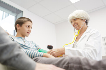 mature pediatrician examining boy with stethoscope