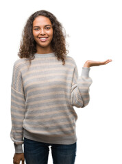 Beautiful young hispanic woman wearing stripes sweater smiling cheerful presenting and pointing with palm of hand looking at the camera.