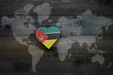 wooden heart with national flag of mozambique near world map on the wooden background.