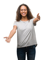 Beautiful young hispanic woman wearing glasses looking at the camera smiling with open arms for hug. Cheerful expression embracing happiness.
