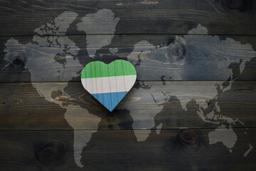 wooden heart with national flag of sierra leone near world map on the wooden background.