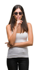 Naklejka premium Young beautiful hispanic wearing sunglasses asking to be quiet with finger on lips. Silence and secret concept.