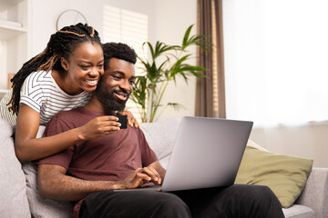 Joyful African American couple using a credit card to shop online, sitting comfortably on the couch at home.