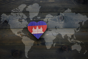 wooden heart with national flag of cambodia near world map on the wooden background.