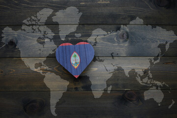 wooden heart with national flag of guam near world map on the wooden background.