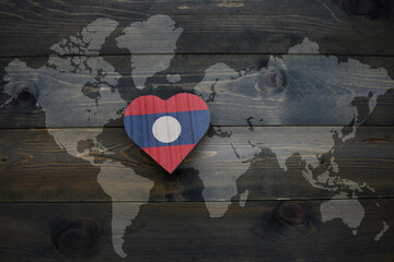 wooden heart with national flag of laos near world map on the wooden background.