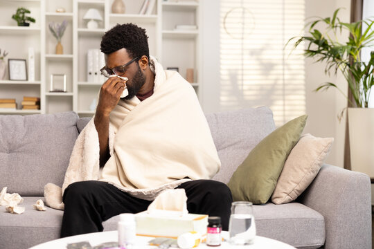 Sick Man With Cold and Flu Resting On Couch, Surrounded By Medicines and Tissues, Indoor Illness Concept.