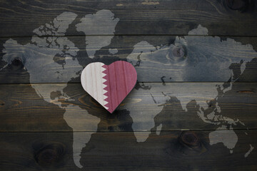 wooden heart with national flag of qatar near world map on the wooden background.