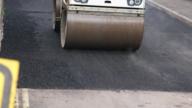 A road roller machine flattening newly laid tarmac road in slow motion
