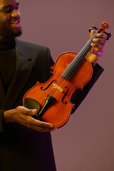 Elegant man in black suit holding violin against purple background with another man
