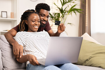 Affectionate couple engaged in online shopping, using a credit card and laptop while sitting...