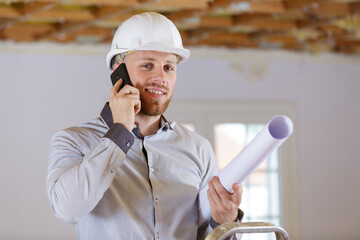 male architect holding rolled up plans and talking on telephone - obrazy, fototapety, plakaty
