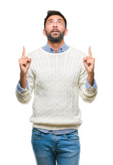 Adult hispanic man wearing winter sweater over isolated background amazed and surprised looking up and pointing with fingers and raised arms.