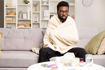 Sick Man Feeling Unwell On Couch With Medicine And Water. A Young Male With Glasses Wrapped In A...