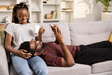 Happy Couple Relaxing On Couch, Woman Laughing Holding Coffee, Man Lying Down Enjoying Smartphone, Cozy Home Setting