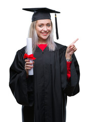 Young blonde woman wearing graduate uniform holding degree over isolated background very happy pointing with hand and finger to the side