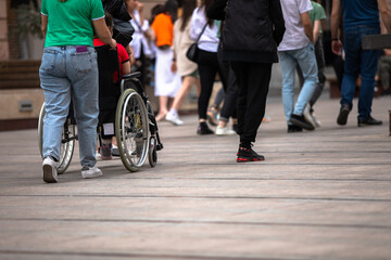 Woman walking on a crowded city street with her husband in a wheelchair, the lifestyle of a disabled person, stock photo