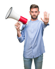 Young handsome man yelling through megaphone over isolated background with open hand doing stop sign with serious and confident expression, defense gesture