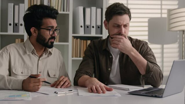 Two diverse anxious displeased businessmen Arabian Indian Caucasian men male colleagues coworkers develop business project online together brainstorming working on laptop upset with mistake in office