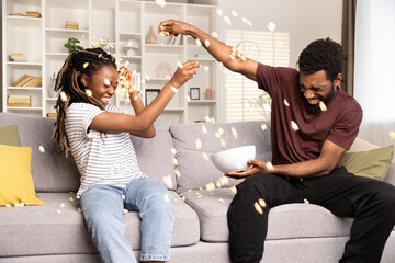 Joyful Couple Having Fun With Popcorn On Couch. African American Man And Woman Enjoying Playful Time, Home Entertainment. Lifestyle, Leisure, Togetherness Concept Captured.  - obrazy, fototapety, plakaty