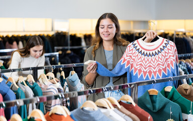 Smiling female in casual outfit admiring pullover with a pattern in a showroom