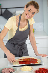 woman adding tomato sauce to pizza base