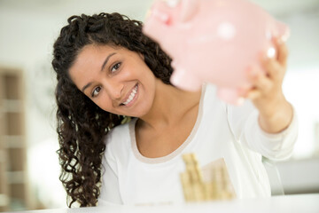 joyous young woman holding piggybank with lots of money