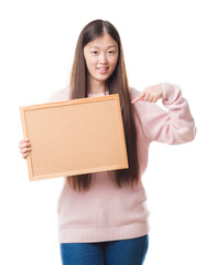 Young Chinese woman over isolated background holding corkboard with surprise face pointing finger to himself