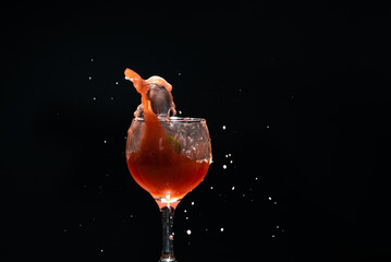 A glass cup with guava juice inside with splashes coming up. Isolated on dark background.