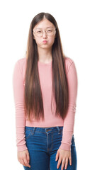 Obraz premium Young Chinese woman over isolated background wearing glasses puffing cheeks with funny face. Mouth inflated with air, crazy expression.