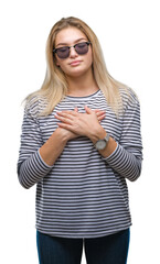 Fototapeta premium Young caucasian woman wearing sunglasses over isolated background smiling with hands on chest with closed eyes and grateful gesture on face. Health concept.