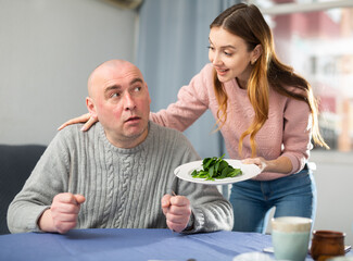Woman made salad and serving it for her husband who sitting at table.