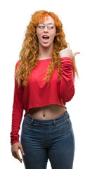 Young redhead woman wearing glasses pointing and showing with thumb up to the side with happy face...