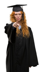 Young redhead student woman wearing graduated uniform pointing with finger to the camera and to you, hand sign, positive and confident gesture from the front