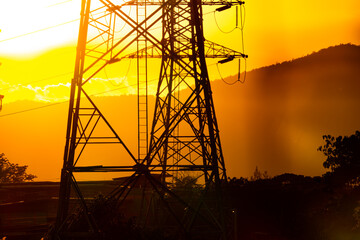 A tall power tower is silhouetted against a sunset