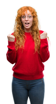 Young redhead woman wearing red sweater celebrating surprised and amazed for success with arms raised and open eyes. Winner concept.