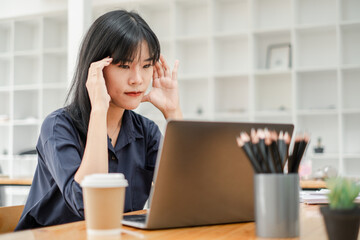 Young professional appears stressed and tired as she works on her laptop, trying to meet deadlines...