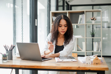 Real estate agent examines property documents while working on a laptop in a modern office, with...