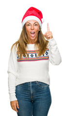 Middle age adult woman wearing winter sweater and chrismat hat over isolated background pointing finger up with successful idea. Exited and happy. Number one.