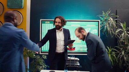 Project manager welcoming his team in business meeting, shaking hands. Supervisor explains the overall enterprise goals, analyzing the current situation and works through planning details. Camera B.