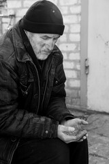 Poor homeless senior man holding coins outdoors. Black and white effect