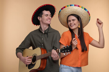 Lovely couple woman in Mexican sombrero hats playing guitar on beige background