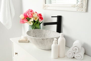Vase with beautiful pink tulips and toiletries near sink in bathroom