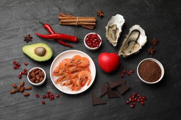 Natural aphrodisiac. Different food products and heart model on black table, flat lay