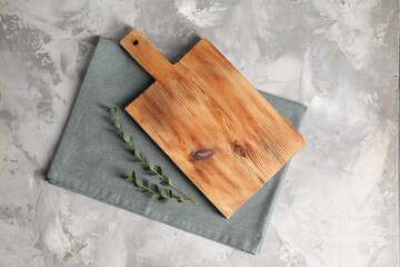 Wooden cutting board, green branch and napkin on grey table, top view