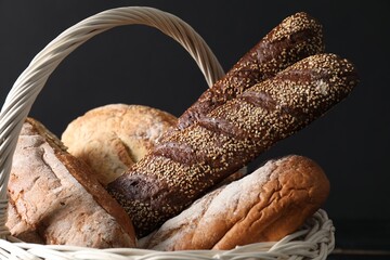 Wicker basket with different types of fresh bread on dark background, closeup