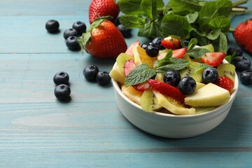 Tasty fruit salad in bowl and ingredients on light blue wooden table, closeup