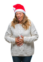 Middle age senior hispanic woman wearing christmas hat over isolated background with hand on stomach because indigestion, painful illness feeling unwell. Ache concept.
