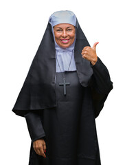 Middle age senior christian catholic nun woman over isolated background smiling with happy face looking and pointing to the side with thumb up.